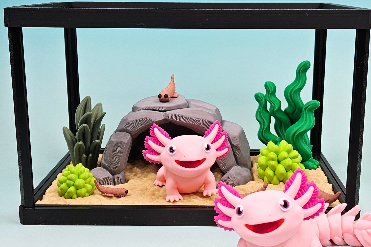 Pink axolotl figurines in a small aquarium with rocks and plants on a light blue background.